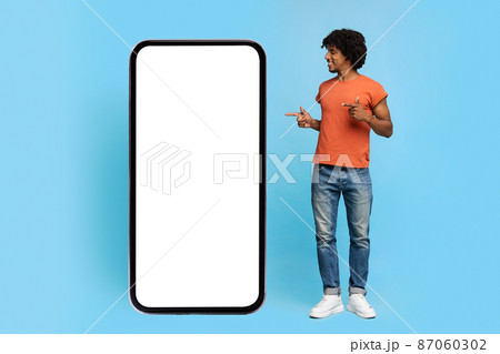 Positive black guy standing by big smartphone with blank screen Positive black guy standing by big smartphone with blank screen 87060302