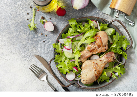 Healthy clean eating. Meat with fresh salad. Baked chicken drumsticks and a green vegan salad made from a of green leaves and spring vegetables on a stone countertop. Top view flat lay. Copy space. 87060495