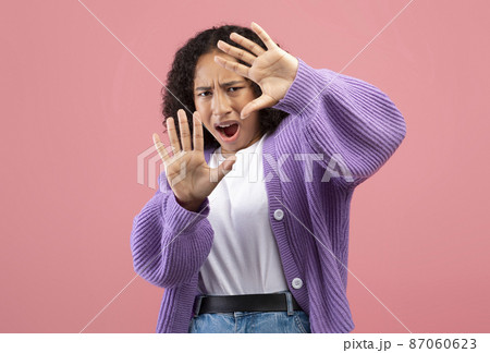 Young African American woman feeling scared, shouting in fear, trying to protect herself with hands on pink background Young African American woman feeling scared, shouting in fear, trying to protect herself with hands on pink background 87060623