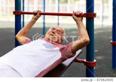 Open air gym. Street training on the municipal sports equipment. Elderly man pumps the press in city park 87062600