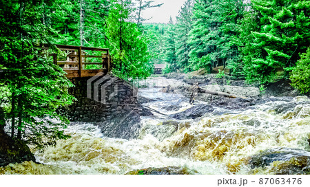 Flooding waters at the waterfalls with tree stump. Flooding waters at the waterfalls with tree stump. 87063476