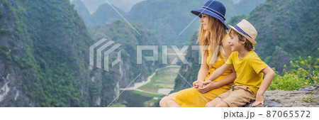 BANNER, LONG FORMAT Mother and son tourists on the lake Tam Coc and pagoda of Hang Mua temple, Ninh Binh, Viet nam. It's is UNESCO World Heritage Site, renowned for its boat cave tours. It's Halong 87065572