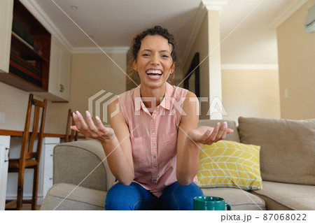 Portrait of cheerful young biracial woman gesturing during video call while sitting on sofa at home 87068022