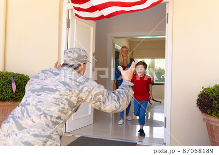 Caucasian mid adult woman looking at caucasian son running to mid adult male soldier at doorway Caucasian mid adult woman looking at caucasian son running to mid adult male soldier at doorway 87068189