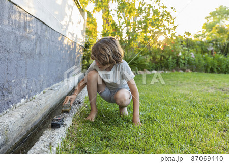 Boy (8-9) with toy cars in garden Boy (8-9) with toy cars in garden 87069440