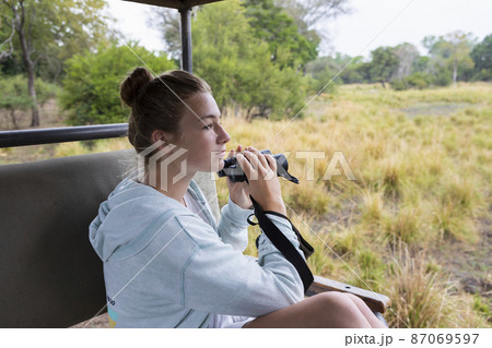 Africa, Zambia, Livingstone, Girl (16-17) in safari vehicle using binoculars Africa, Zambia, Livingstone, Girl (16-17) in safari vehicle using binoculars 87069597