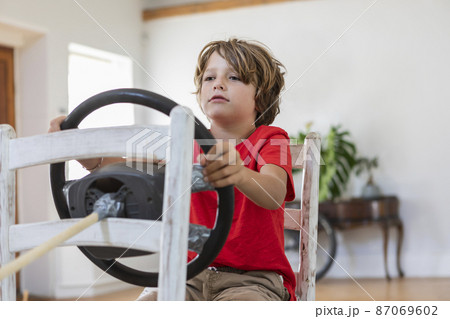 Boy (8-9) playing with steering wheel in living room Boy (8-9) playing with steering wheel in living room 87069602