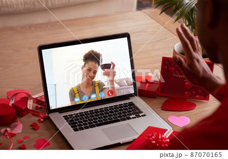 Smiling biracial young woman with red wine during online dating with boyfriend on valentine day 87070165