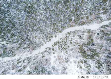 Aerial view of the road in the winter forest with high pine or spruce trees covered by snow. Driving in winter. Aerial view of the road in the winter forest with high pine or spruce trees covered by snow. Driving in winter. 87070976