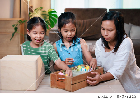 Asian mother and her daughters are decorating easter eggs preparing for Easter at home. Happy family Happy easter Happy holiday. 87073215
