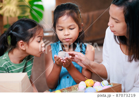 Asian mother and her daughters are playing with baby bunny and decorating easter eggs preparing for Easter at home. Happy family Happy easter Happy holiday. 87073219