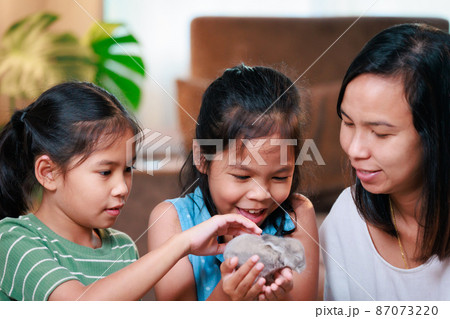 Asian mother and her daughters are playing with baby bunny and decorating easter eggs preparing for Easter at home. Happy family Happy easter Happy holiday. 87073220