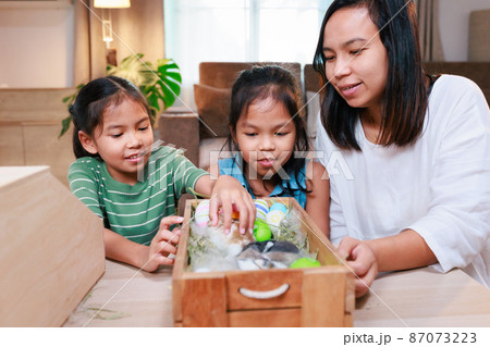 Asian mother and her daughters are playing with baby bunny and decorating easter eggs preparing for Easter at home. Happy family Happy easter Happy holiday. 87073223