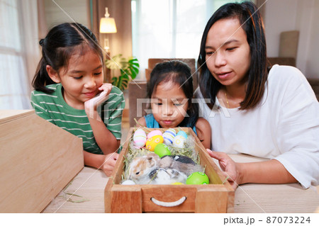 Asian mother and her daughters are playing with baby bunny and decorating easter eggs preparing for Easter at home. Happy family Happy easter Happy holiday. Asian mother and her daughters are playing with baby bunny and decorating easter eggs preparing for Easter at home. Happy family Happy easter Happy holiday. 87073224