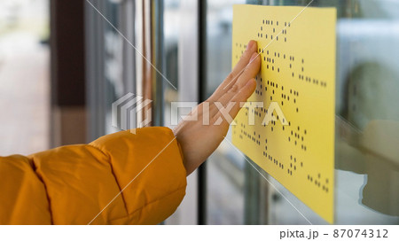 Close-up of a woman reading a braille lettering on a glass door. Close-up of a woman reading a braille lettering on a glass door. 87074312