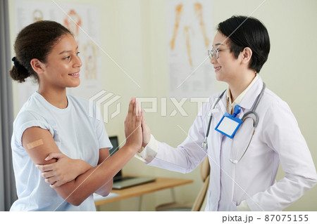Asian female doctor in white coat giving the high-five to the girl after she getting vaccine at hospital Asian female doctor in white coat giving the high-five to the girl after she getting vaccine at hospital 87075155