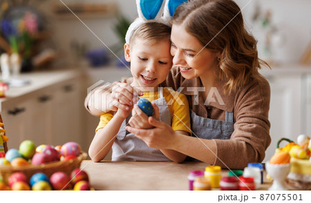 Loving young mother teaching happy little kid son to decorate Easter eggs while sitting in kitchen Loving young mother teaching happy little kid son to decorate Easter eggs while sitting in kitchen 87075501