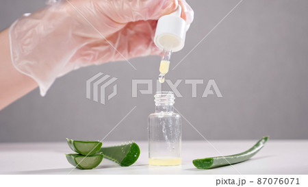 Specialist drops aloe juice into glass bottle on white table 87076071