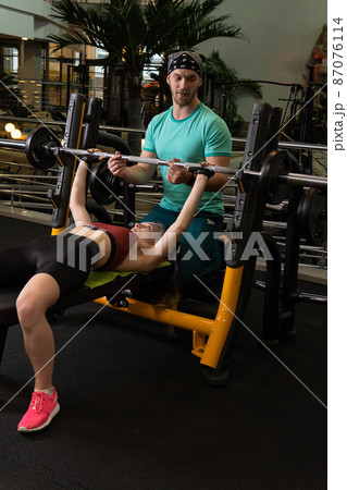 Instructor led training helps a beautiful client to perform exercises in a fitness club, the concept of playing sports with a professional gym leisure lifestyle mature modern, from personal retiree 87076114