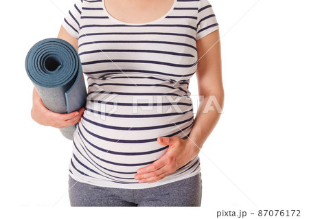 Pregnant woman standing with yoga mat 87076172