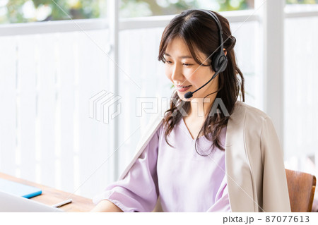 屋内でヘッドセットをつけてノートパソコンに向かうビジネスウーマン 屋内でヘッドセットをつけてノートパソコンに向かうビジネスウーマン 87077613