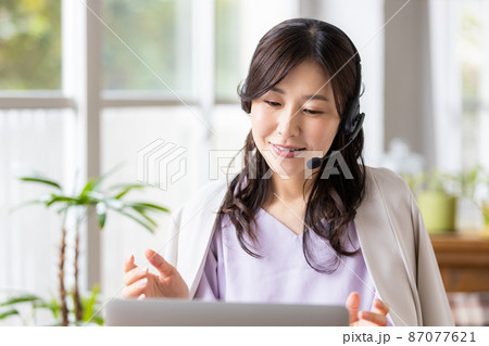 屋内でヘッドセットをつけてノートパソコンに向かうビジネスウーマン 87077621