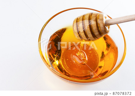 Sweet honey. Healthy organic honey dripping from wooden honey dipper in a bowl on white background. Sweet healthy dessert. 87078372