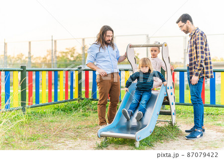 Little boy playing on slider of playground with his family 87079422