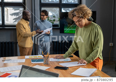 Young female economist looking through financial data by table Young female economist looking through financial data by table 87080295
