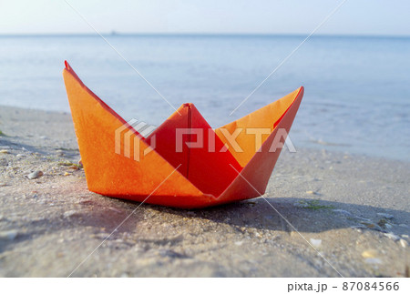 Small paper orange boat on sand near water on background of sea waves 87084566