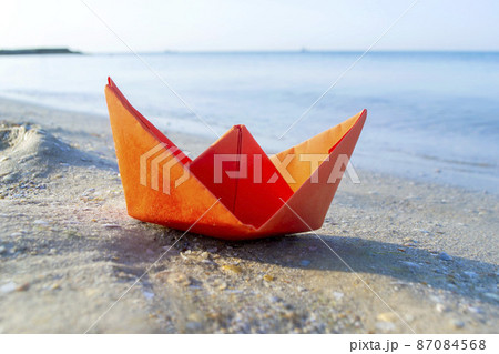 Small paper orange boat on sand near water on background of sea waves 87084568