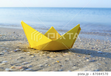 Small paper yellow boat on sand near water on background of sea waves 87084570
