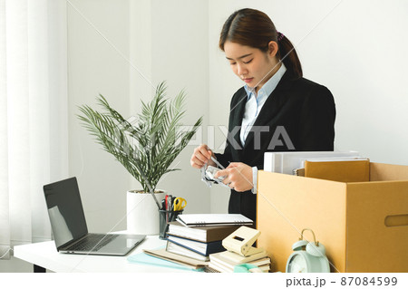 A woman office worker is unhappy with being fired from a company packing things into cardboard boxes. The Young woman was stressed and disappointed by being fired. concept of layoffs and unemployment 87084599