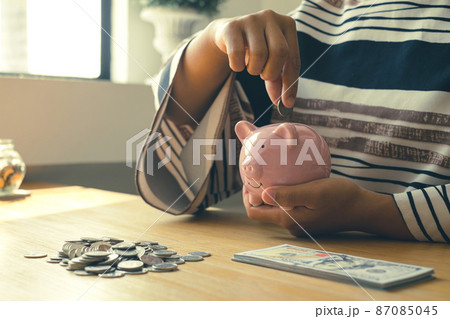 Woman's hand. putting coins in the piggy bank with coins, saving money with coins, stepping into a successful growing business, and saving for thought in retirement. Retirement savings concept Woman's hand. putting coins in the piggy bank with coins, saving money with coins, stepping into a successful growing business, and saving for thought in retirement. Retirement savings concept 87085045