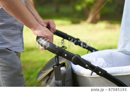 A young dad walking in the park with a baby in a stroller. Close-up of men's hands with a stroller. Father's Day concept. High quality photo 87085193