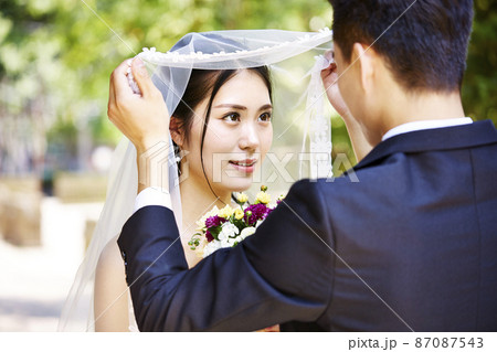 asian groom lifting up bridal veil to kiss beautiful bride 87087543