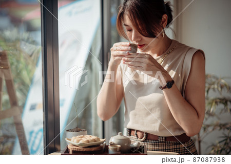An Asian woman is sniffing tea and has a set of Roasted Mitarashi Dango in front of her. An Asian woman is sniffing tea and has a set of Roasted Mitarashi Dango in front of her. 87087938