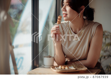 An Asian woman is tasting a Roasted Mitarashi Dango. 87087939