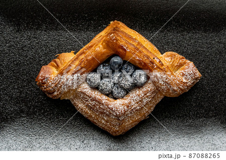 dessert is a small puff pastry pie with stuffing inside on a black serving plate on a black background . A piece of cake with a cut 87088265