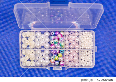 Transparent plastic container with beads and beads of different sizes, blue background 87088486