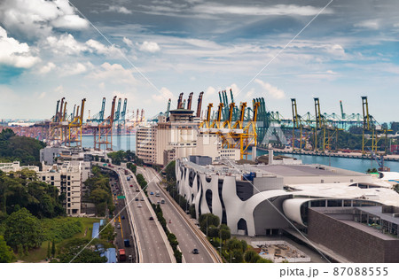 The huge busiest logistic port in Singapore, plenty of cranes to move containers, huge cargo ships in the background, shopping malls and skyscrapers surrounded by, entertainment island nearby 87088555