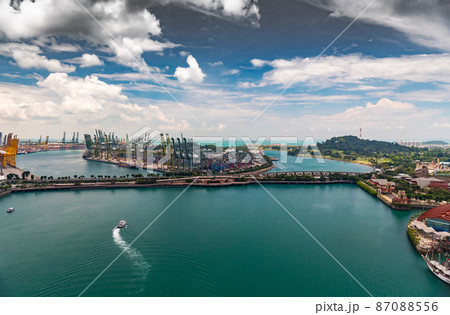 The huge busiest logistic port in Singapore, plenty of cranes to move containers, huge cargo ships in the background, shopping malls and skyscrapers surrounded by, entertainment island nearby 87088556