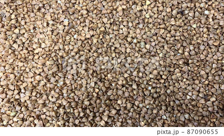 Buckwheat tea in a wooden spoon on a light wooden background. Buckwheat tea close-up macro photography. Scattered buckwheat tea pellets on wooden background 87090655