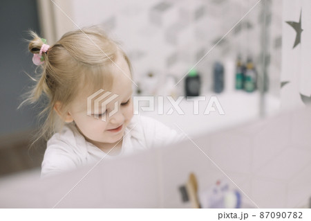 little funny girl brushing teeth and washing hands in the bathroom, reflection in the mirror. little funny girl brushing teeth and washing hands in the bathroom, reflection in the mirror. 87090782