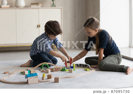 Two focused kids building toy railroad on floor, completing construction Two focused kids building toy railroad on floor, completing construction 87095730