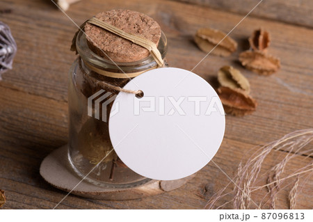 Round white tag mockup on glass jar with dry perfume a wooden background with boho decoration, element for packing 87096813
