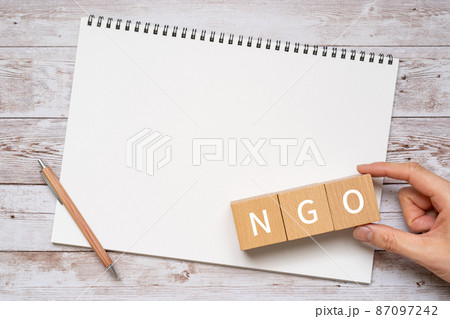 NGOのイメージ｜「NGO」と書かれた積み木、ペン、ノート、人の手 87097242