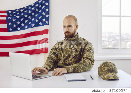 American military student sitting at table and working on his notebook PC. Serious focused shaven headed young man who serves in US army using laptop computer for studying. Military education concept 87100574