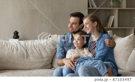 Dreamy parents and sweet daughter girl sitting on couch Dreamy parents and sweet daughter girl sitting on couch 87103497