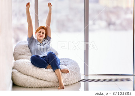 Housewarming in unfurnished apartment by young woman who sits on chair. 87103802